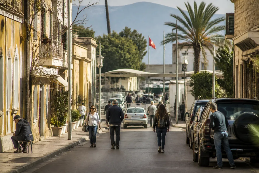 Blick auf die geteilte Stadt Nikosia mit moderner Straße, Menschen im Alltag und Zypern-Flaggen im Hintergrund