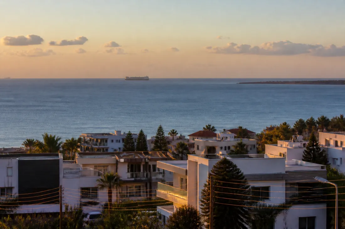 Blick auf die Küste von Zypern mit Stromleitungen und Frachtschiff im östlichen Mittelmeer bei Abendlicht