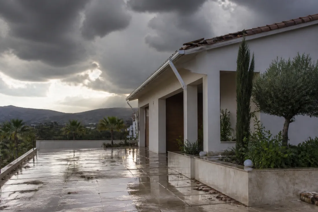 Sturmschäden an einem Haus auf Zypern nach starkem Gewitter mit dunklen Wolken, beschädigter Dachrinne und nasser Einfahrt