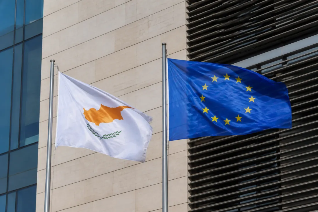 EU-Flagge und zyprische Flagge vor einem modernen Verwaltungsgebäude in Nikosia als Symbol für EU-Gelder und staatliche Umsetzung auf Zypern